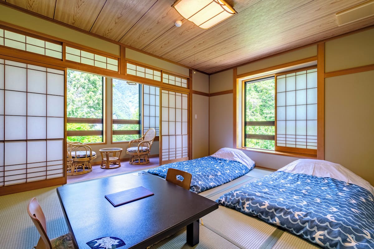 Una habitación japonesa tradicional con suelo de tatami, una mesa baja, dos futones de tatami y puertas correderas.