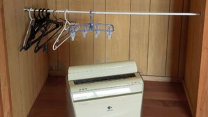 A small room with wooden walls, a white washing machine, a drying rack with clothes, and a blue curtain.