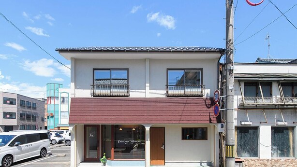 A two-story building with a red awning, a visible entrance, and a small window on the ground floor.
