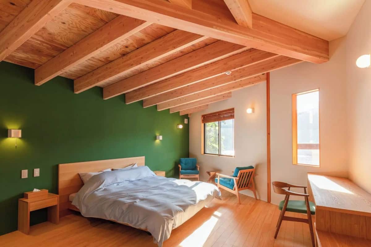 A bedroom with a wooden ceiling, a bed, a desk, and a chair.