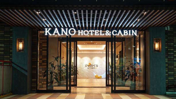 La entrada a KANO HOTEL & CABIN, con un diseño moderno, presenta un fachada de vidrio y un interior acogedor.