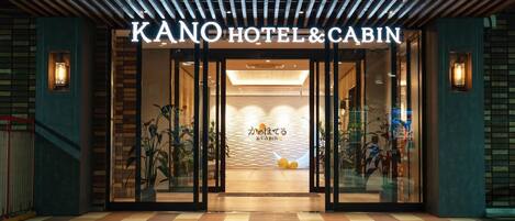 The entrance to KANO HOTEL & CABIN with a modern design, featuring a glass facade and a welcoming interior.