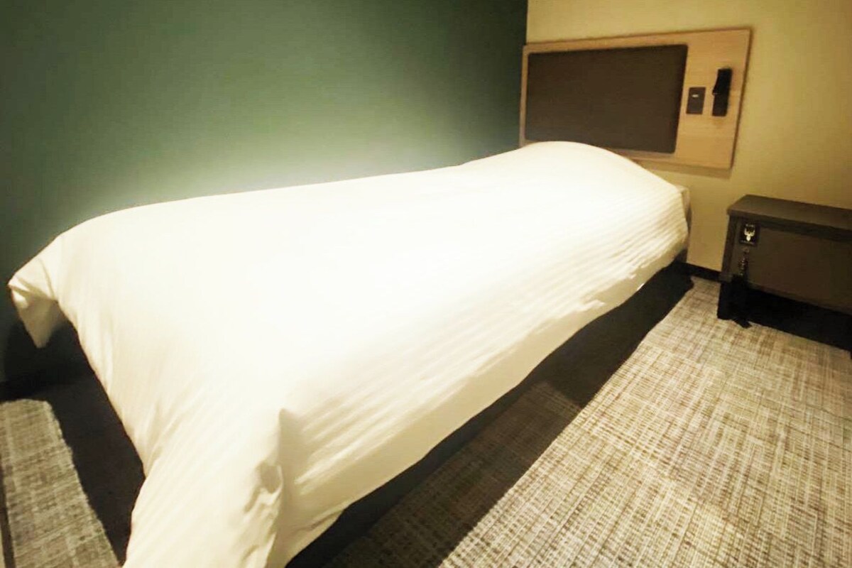A hotel room with a bed, a small bedside table, and a wall-mounted TV.