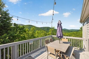 A deck with a table and chairs, a hanging umbrella, and a string of lights. - Blue Ridge Retreat | Hot Tub, Game Room & Views (Fairview)