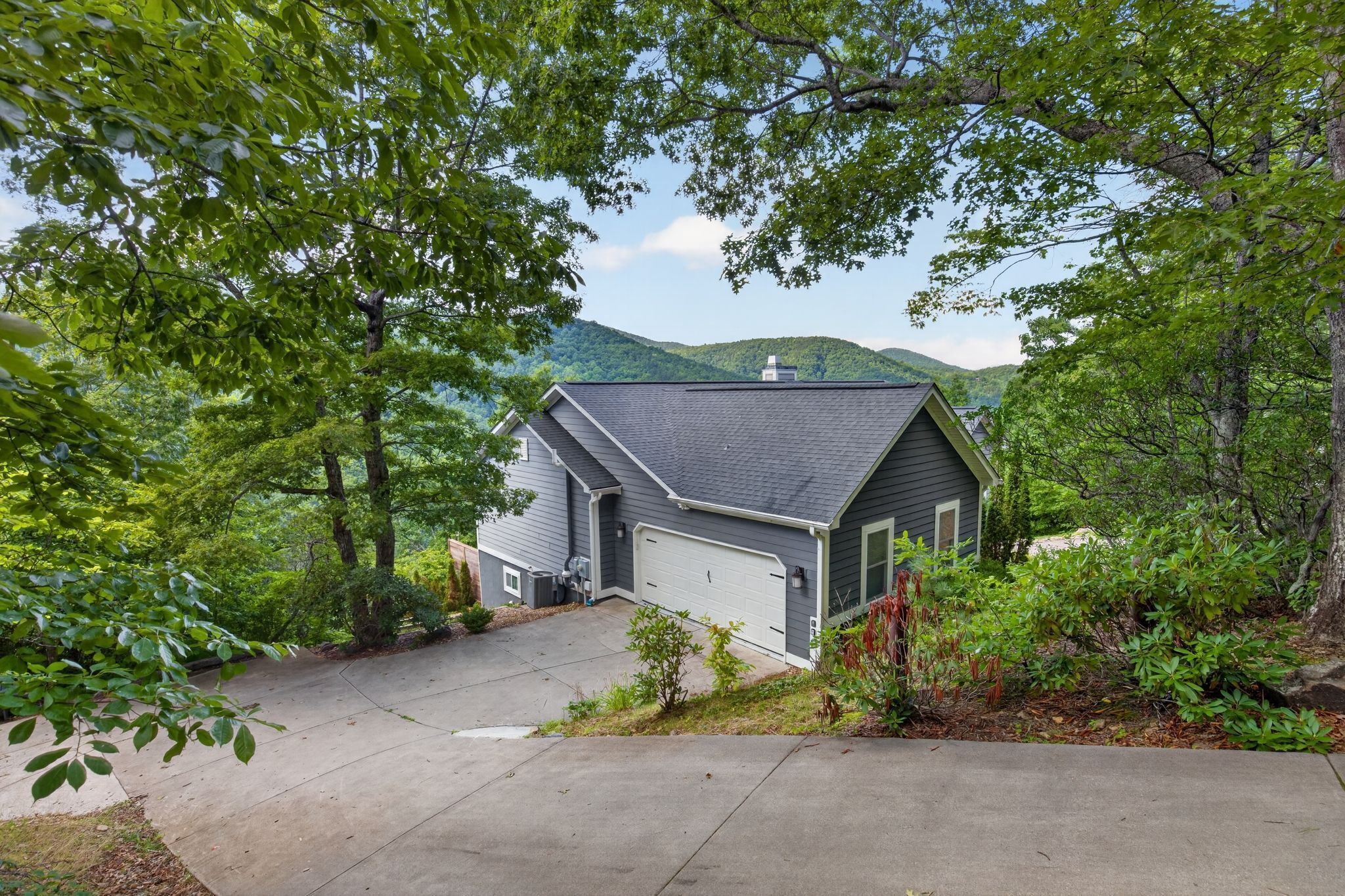 A residential house with a garage, surrounded by trees and a hilly landscape.