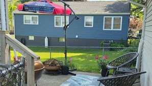 Une maison bleue avec un porche abrité, une chaise en métal, un foyer et un jardin.