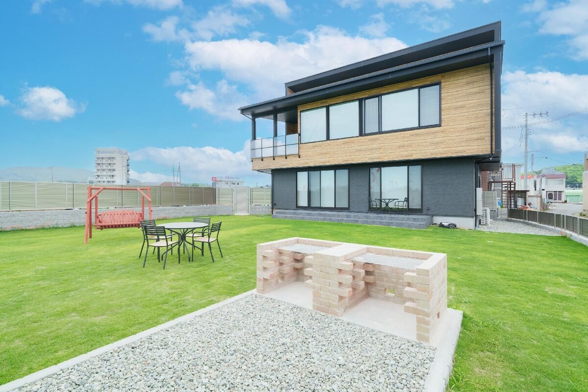 Een modern gebouw met een plat dak, grote ramen en een patio met een tafel en stoelen.