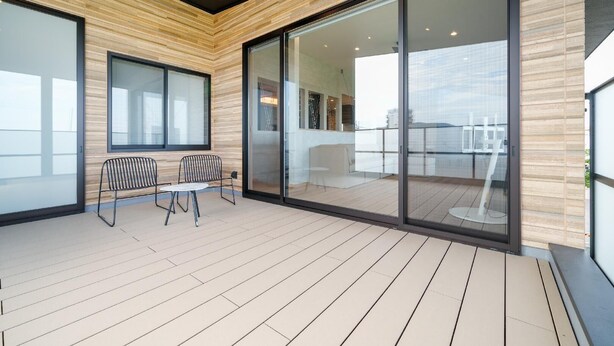 A modern balcony with a wooden floor, two metal chairs, and a glass door leading to an indoor space.