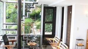Un comedor moderno con una mesa de vidrio y sillas de madera, ventanas amplias y una escalera que lleva a un área exterior.