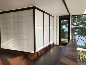 A modern room with a large sliding door, wooden flooring, and a view of a body of water through a large window. - Izu Cliff House (Minamiizu)