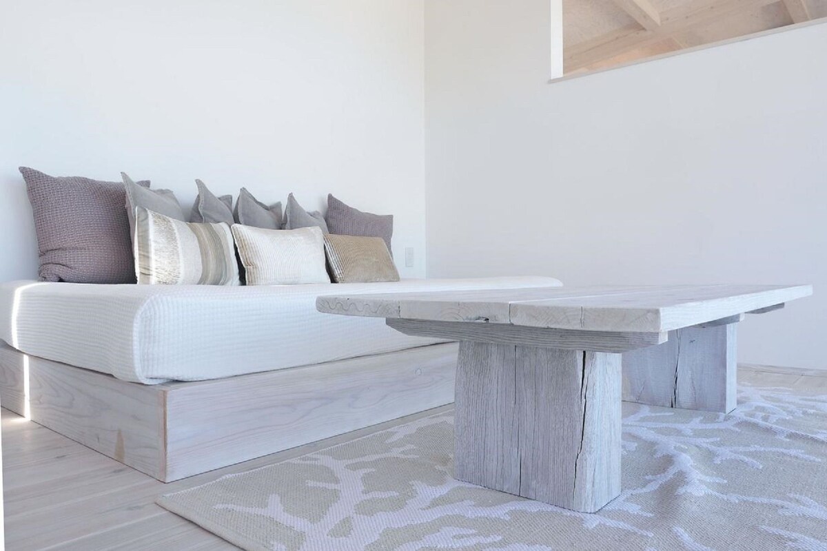 A minimalist bedroom with a bed, a wooden coffee table, and a patterned rug.