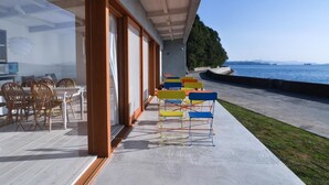 Un espacio moderno para comer al aire libre con vista al mar, sillas de madera y una terraza de concreto.