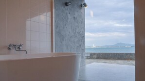 Un baño moderno con una bañera independiente, una pared de mármol y vistas al mar.