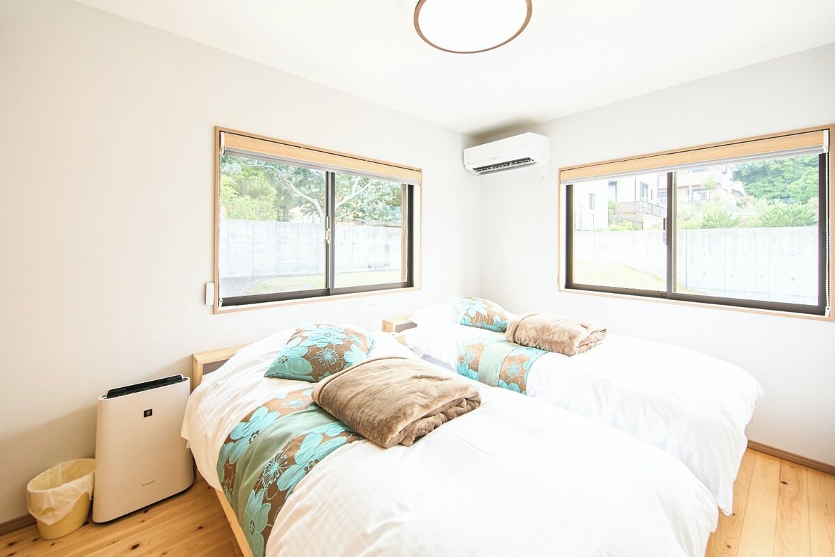 Un dormitorio con dos camas, ventanas amplias, un equipo de aire acondicionado y suelo de madera.