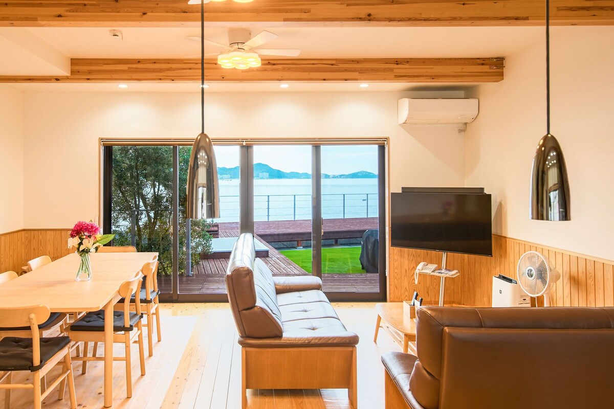 Un interior moderno con una mesa de comedor de madera, sillas, un sofá, un televisor y vistas al mar.