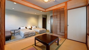 A traditional Japanese-style room with tatami flooring, two beds, a small table, and a sliding door. - Petit Hotel North Inn (Ito)