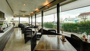 A restaurant with a long counter, multiple tables, and chairs. Large windows provide a view of the outside. - Petit Hotel North Inn (Ito)