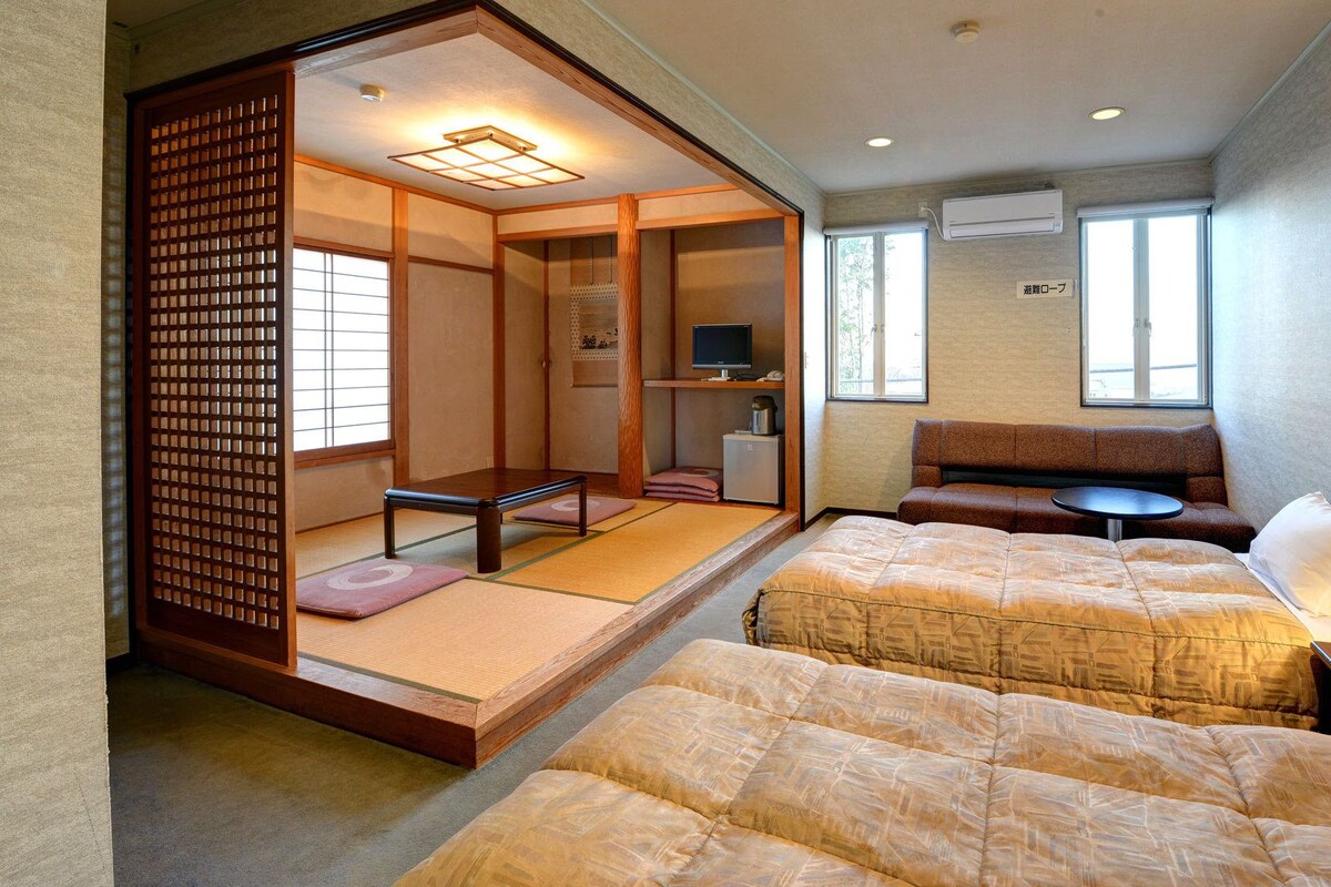 Una camera in stile giapponese tradizionale con pavimento in tatami, un futon, un tavolino con una lampada e un televisore.