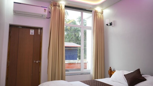 Une chambre d’hôtel équipée d’un lit, de rideaux, d’une fenêtre, d’un climatiseur et d’un luminaire fixé au mur.