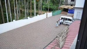 Une cour pavée avec un mur blanc et une clôture verte, une voiture blanche garée et, au fond, un bâtiment avec une enseigne bleue.