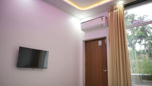 Une chambre d’hôtel équipée d’un lit, d’un téléviseur fixé au mur, d’un appareil de climatisation, d’une porte en bois et d’une fenêtre avec des rideaux.