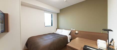 A hotel room with a bed, a desk with a telephone, a small window, and a wall-mounted light.