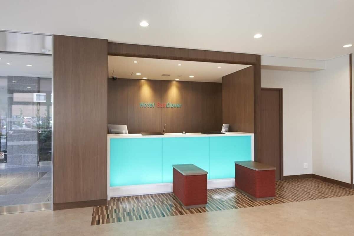 Zona de recepción de un hotel de diseño moderno, con mostrador de recepción, dos taburetes rojos y un cartel en la pared que dice "Hotel SunClove".