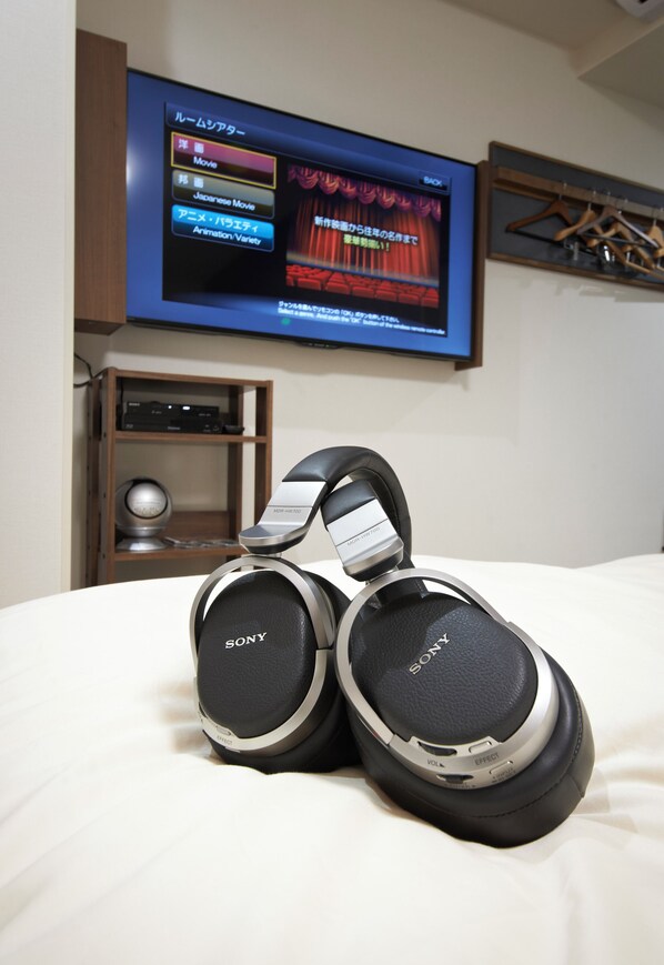 A Sony headphones set on a bed with a TV displaying a movie menu in the background.