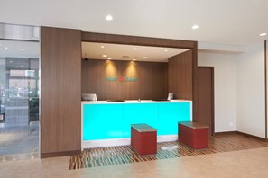 A reception desk with a blue counter, wooden paneling, and two red stools.