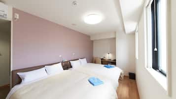 A hotel room with two beds, a desk, a chair, a window, and a ceiling light.
