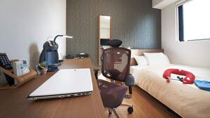 Habitación de hotel con un escritorio de madera, una computadora portátil, una cafetera, una silla, una cama con un almohadón rojo y una ventana.