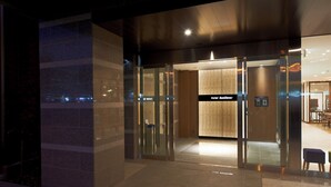 Entrada de un hotel con puerta de vidrio, un letrero que dice 'Hotel SunClover' y un área de recepción visible a través de la puerta.
