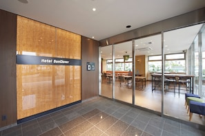 A hotel reception area with a modern design, including a reception desk, a seating area with tables and chairs, and a glass partition.