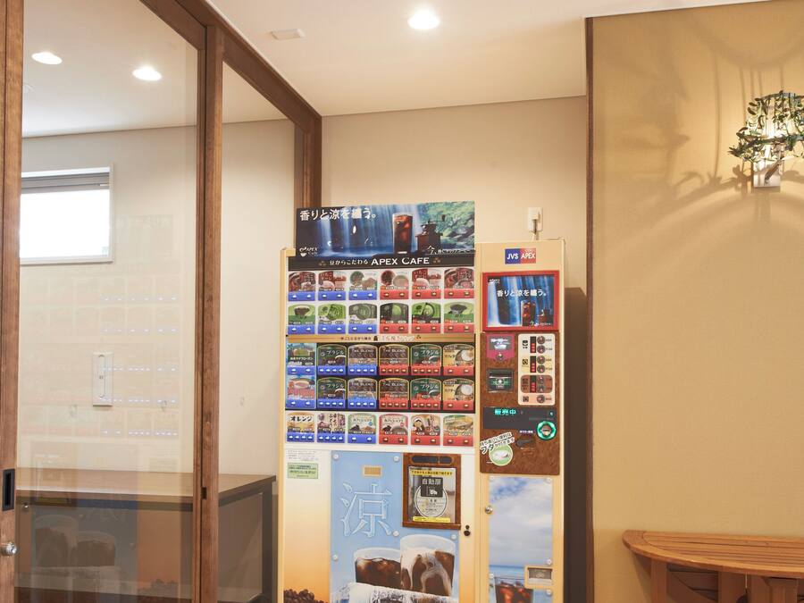 A vending machine with various drink options, a wooden table, and a glass partition.