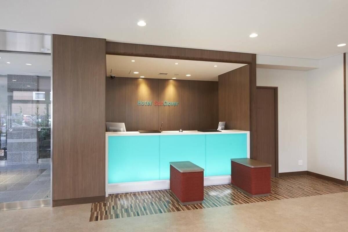 Zona de recepción de un hotel de diseño moderno, con mostrador de recepción, dos taburetes rojos y un cartel en la pared que dice "Hotel SunClove".