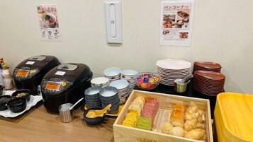 A buffet setup with various food items, serving utensils, and a rice cooker.