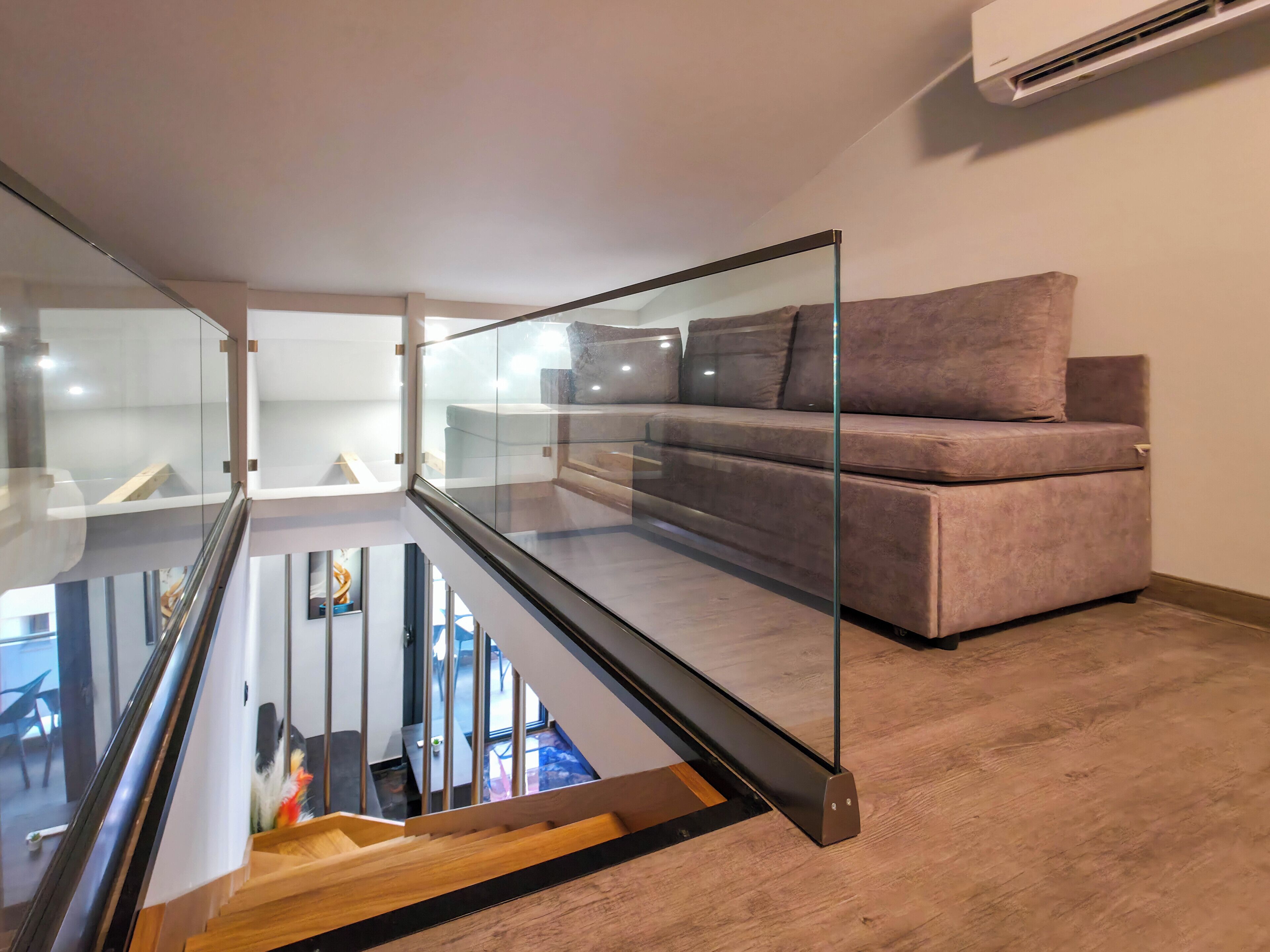 A modern interior with a glass staircase, a sofa, and a wall-mounted air conditioner.