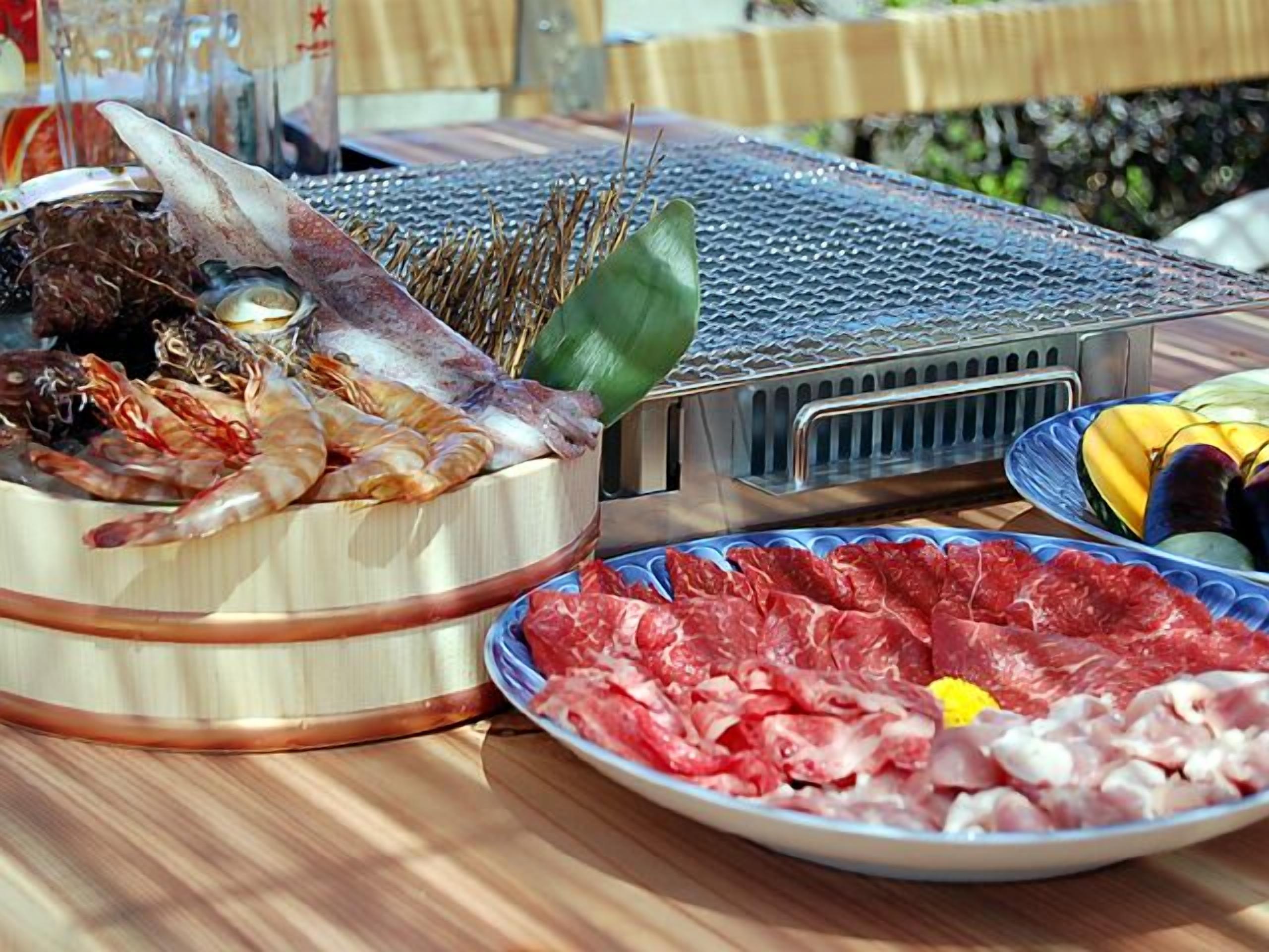 A table with various meats and seafood, a grill, and a plate of bananas.