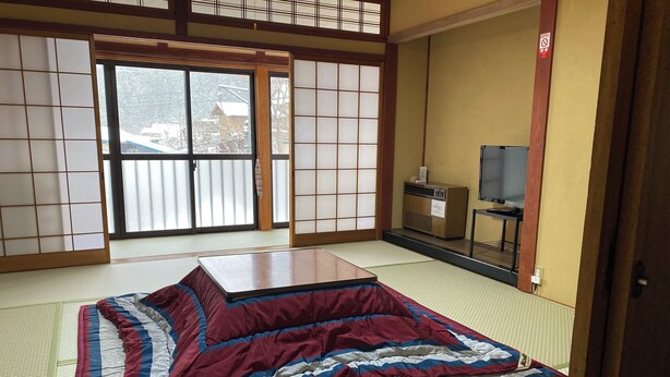 A tatami mat room with a futon bed, sliding doors, a television, and a traditional Japanese cabinet. - Okukannabe Hutte (Toyooka)