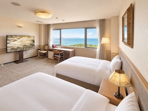 Une chambre d’hôtel avec deux lits, un bureau, une télévision et une vue sur la mer.