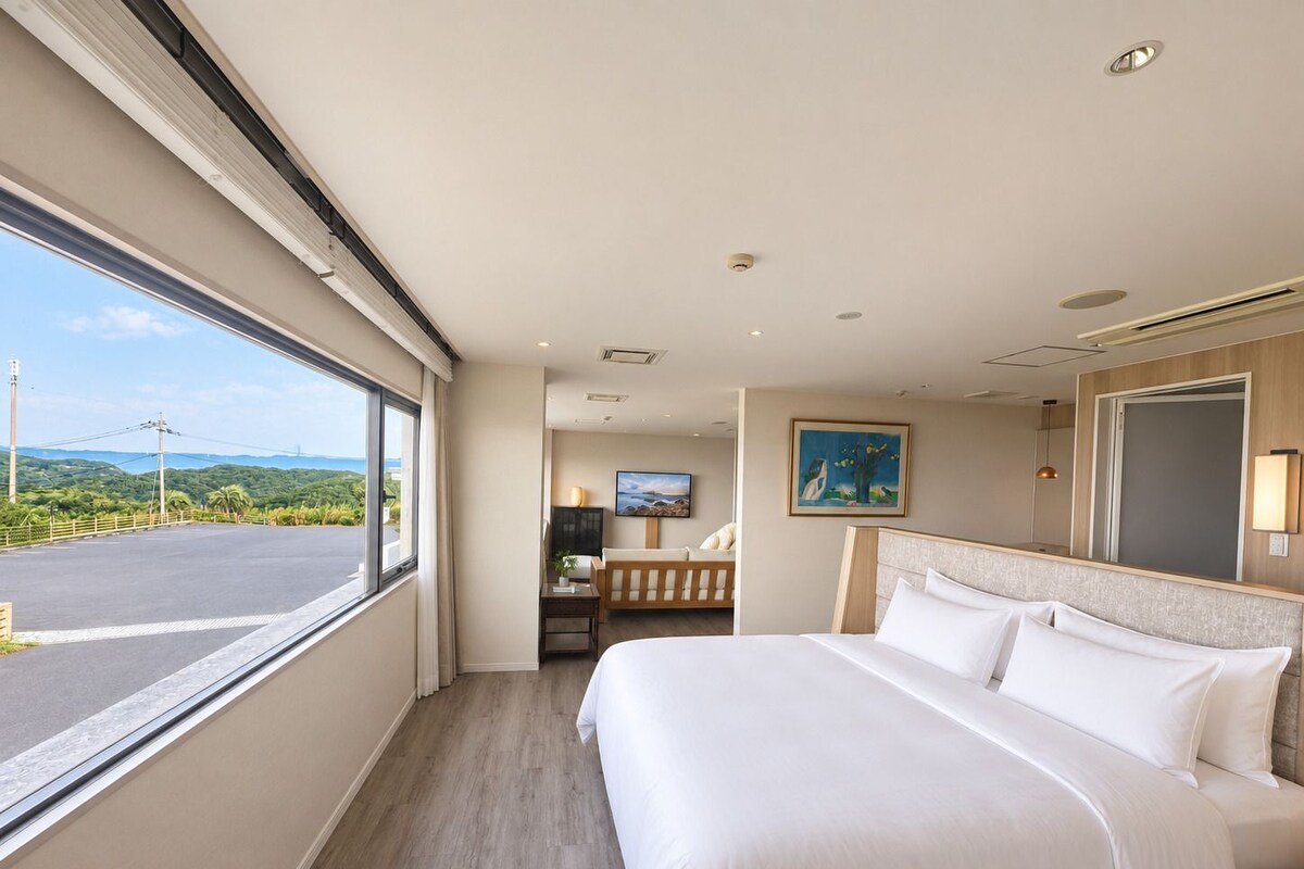 Une chambre d’hôtel avec un grand lit, une télévision, un tableau au mur et une vue sur l’extérieur.