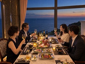 Un groupe de personnes est réuni autour d’une table, d’où l’on peut admirer l’océan, et déguste des plats de fruits de mer accompagnés de vin.