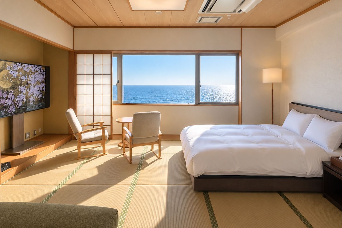 Une chambre d’hôtel avec un lit, une télévision, une vue sur la mer et une porte coulissante de style japonais traditionnel.