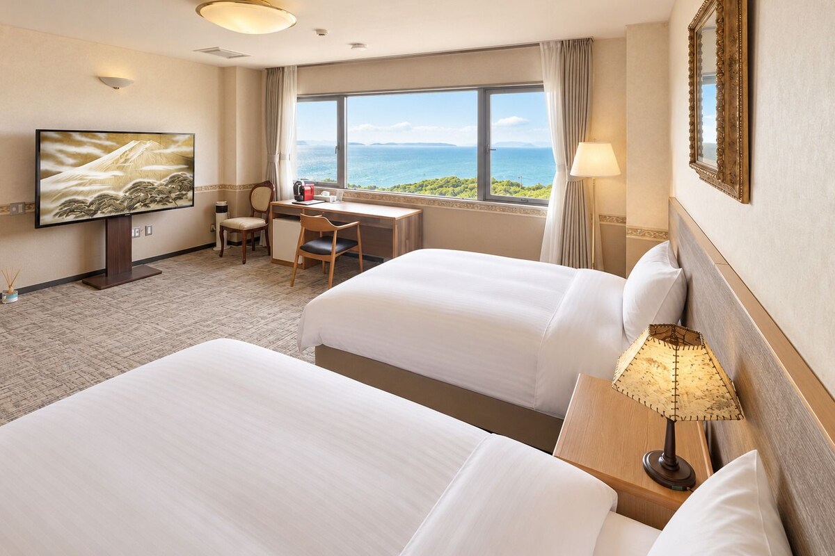 Une chambre d’hôtel avec deux lits, un bureau, une télévision et vue sur la mer.