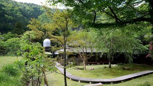Edificio tradicional japonés con techo de paja, rodeado de exuberante vegetación y un sendero de piedra.