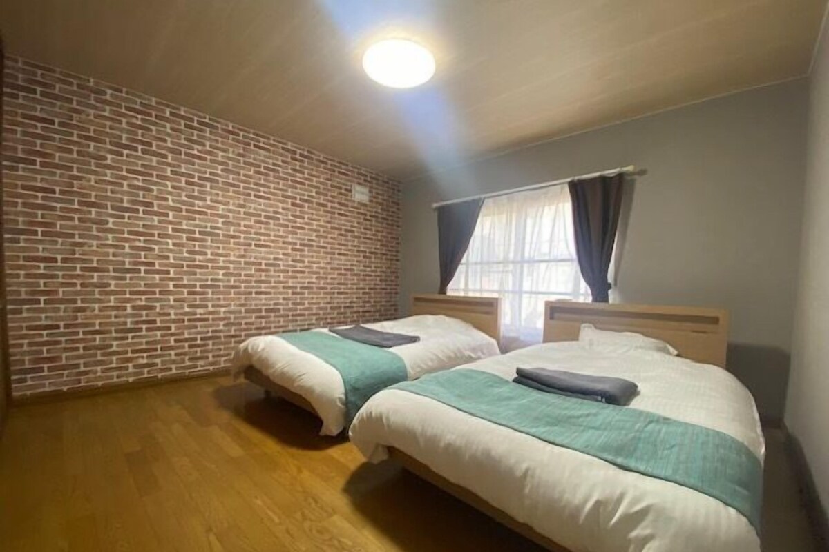 A room with two beds, a brick wall, a wooden floor, and a window with curtains.