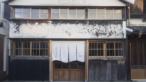 A traditional Japanese building with a two-story facade, large windows, and a wooden door.