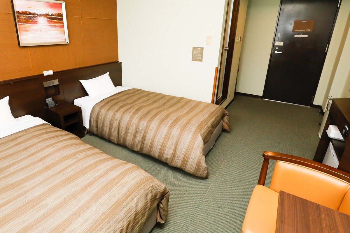 Two beds with striped bedding, a wooden headboard, a nightstand, a chair, and a door with a plaque.