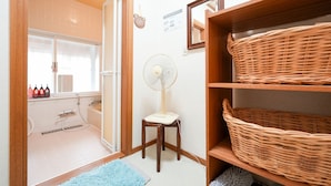 A bathroom with a shower, a fan, a towel rack, and a shelf with baskets. - Pension Mascot (Tsumagoi)