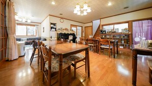 A dining area with wooden furniture, a chandelier, and a kitchen area with a stove and shelves. - Pension Mascot (Tsumagoi)